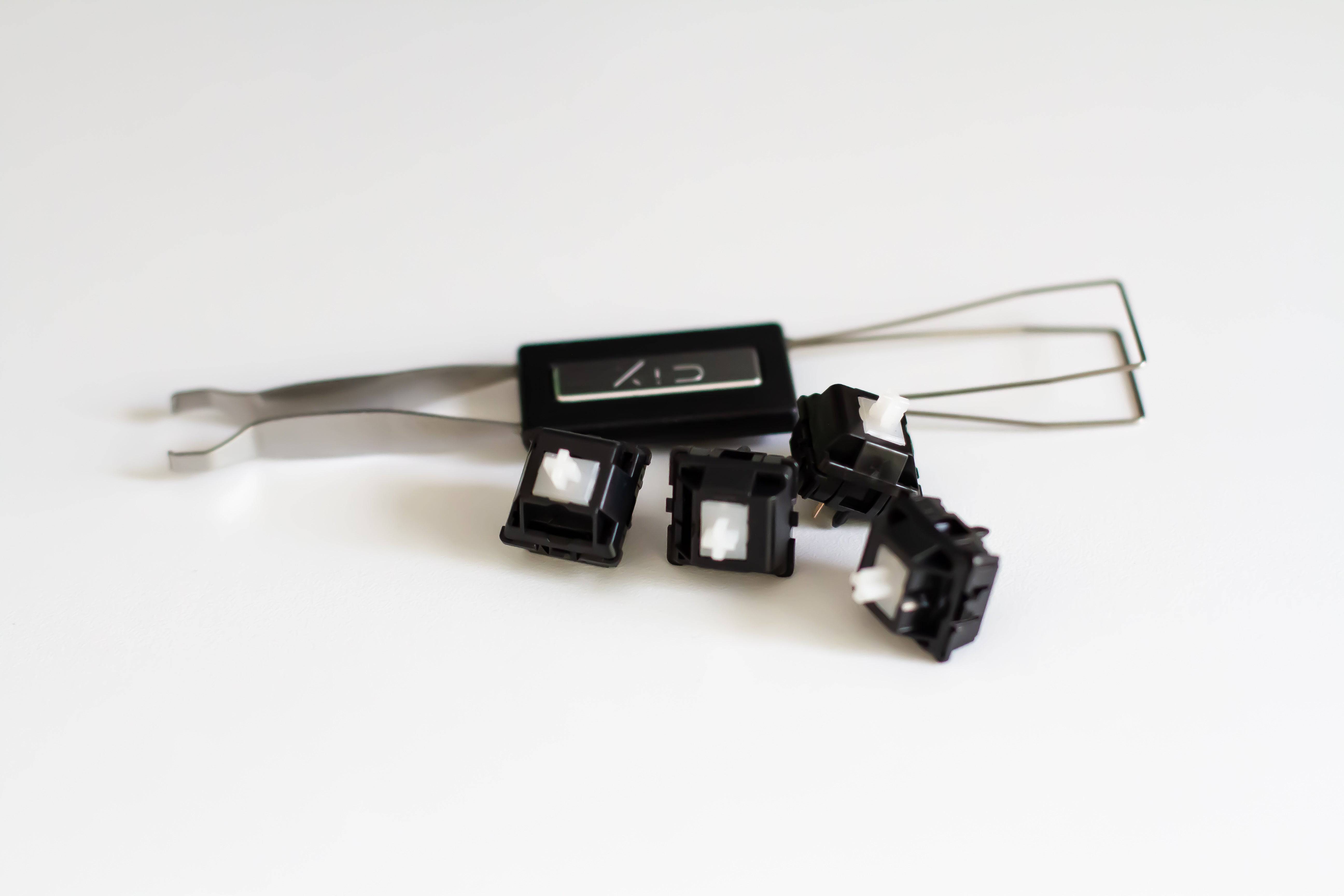 A few Durock POM linear mechanical keyboard switches next to a CY stainless steel switch puller.