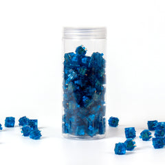 Gateron Blue Ink V2 clicky switches in a clear storage jar with loose blue transparent 5-pin switches