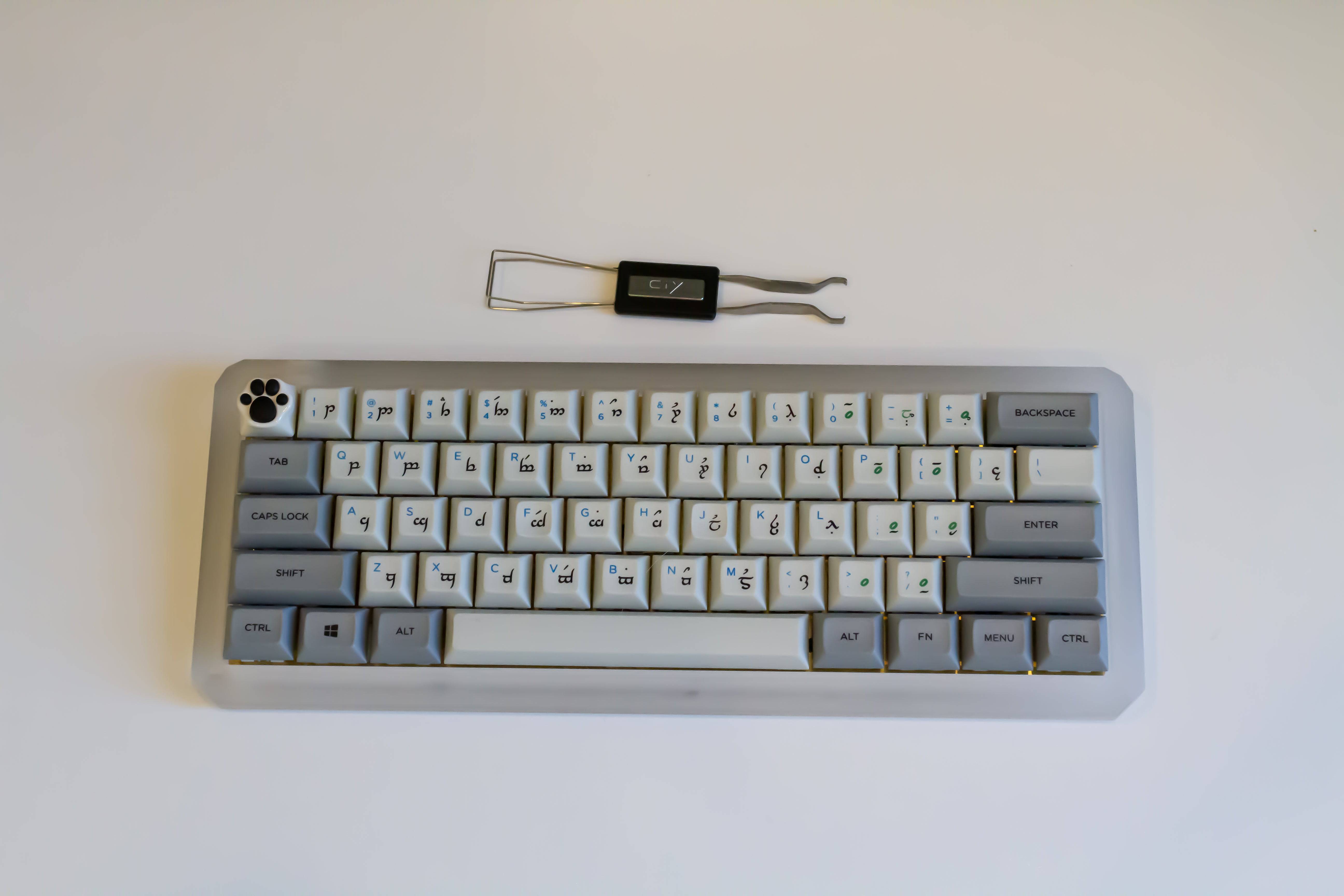 A CY stainless steel mechanical keyboard keycap and switch puller next to a 60% custom mechanical keyboard.