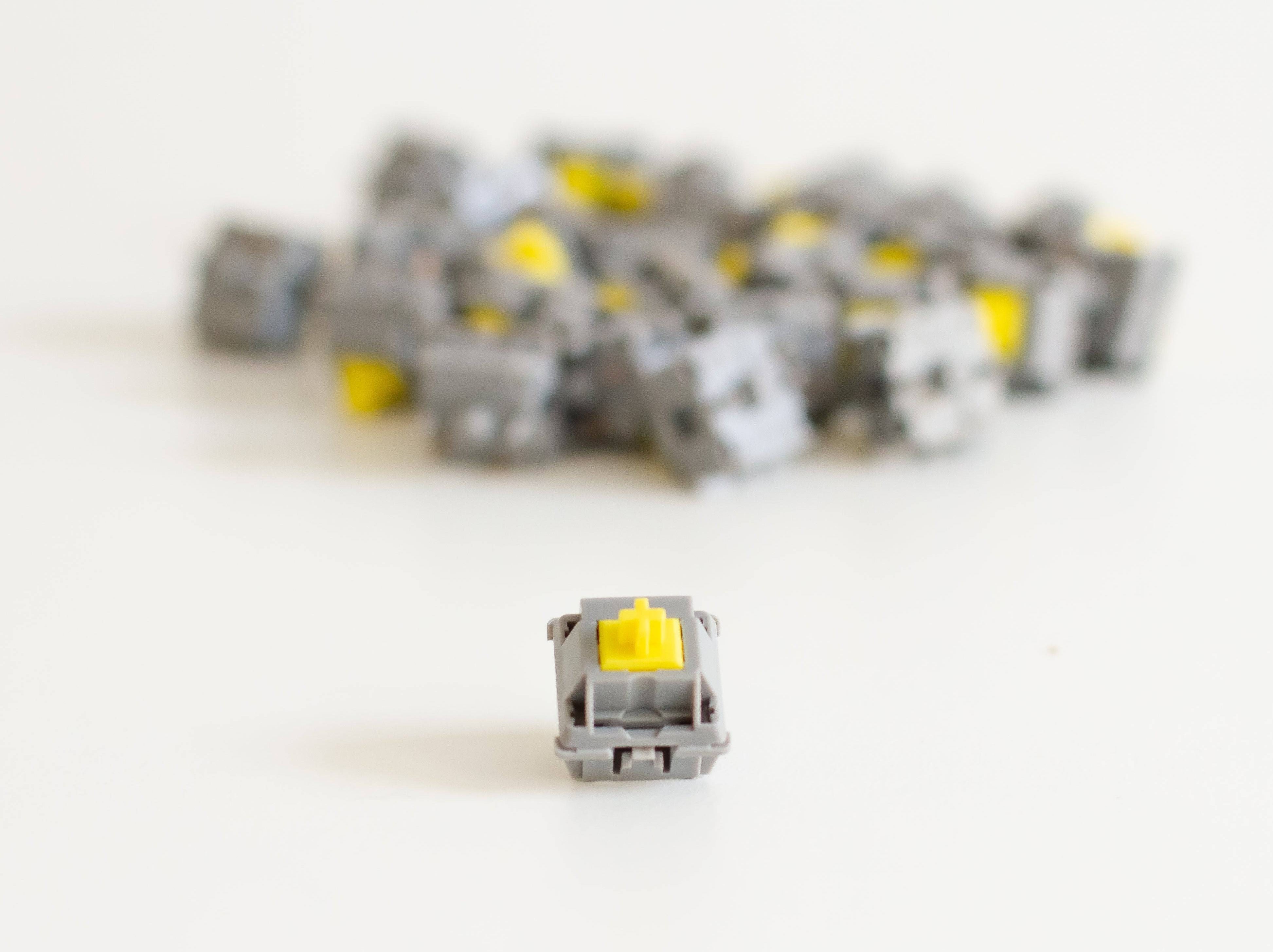 A batch of JWK Durock tactile POM T1 sunflower mechanical keyboard switches with one switch at the front.